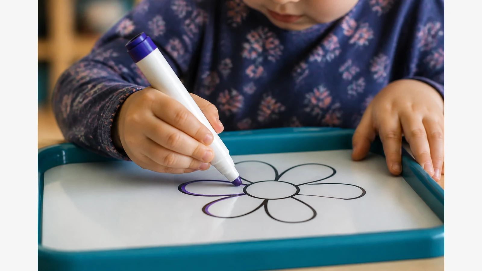 Preschooler practising fine motor control with a marker on a guided drawing tray
